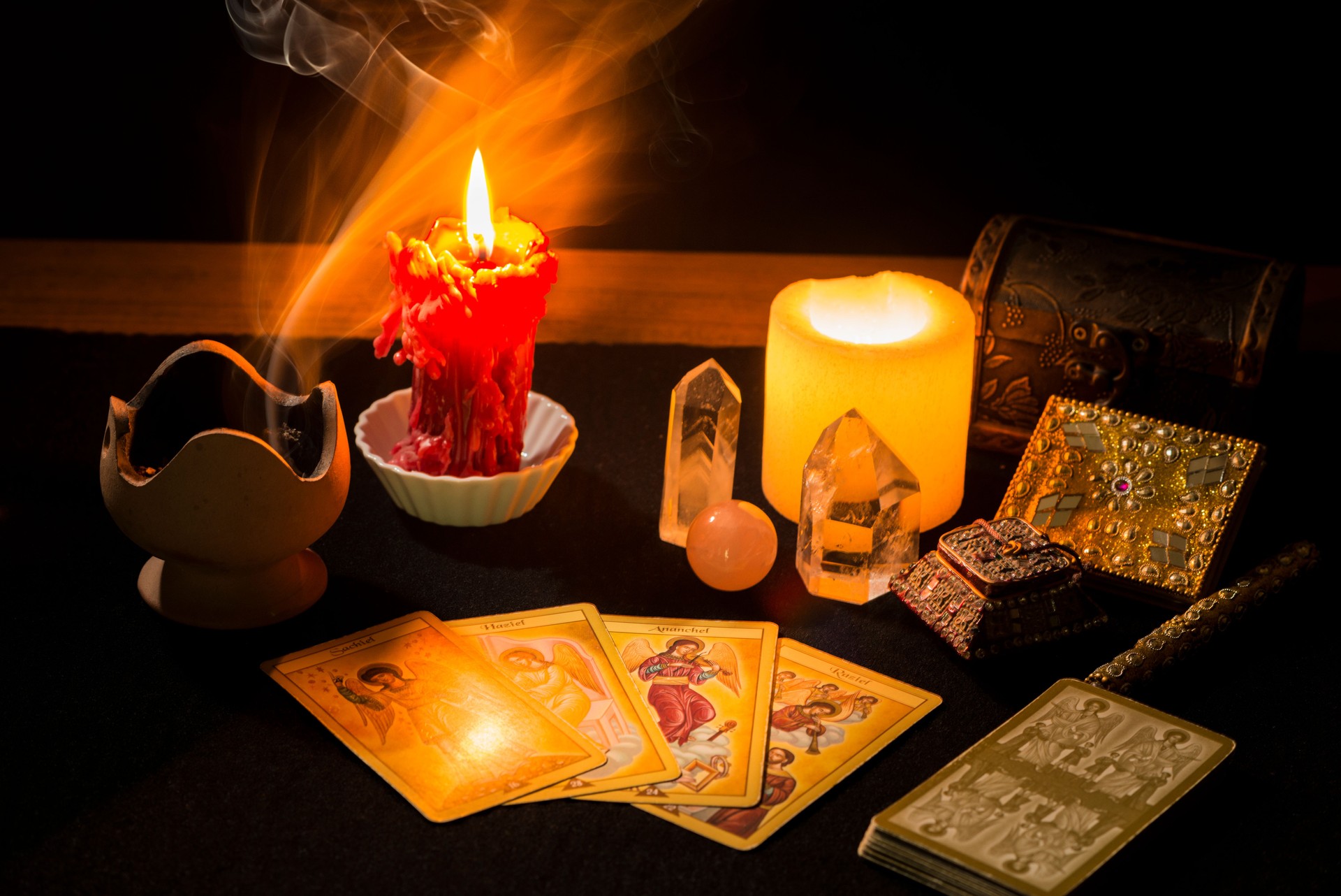 Still life with tarot cards, candles, incense and other objects on a black card table.